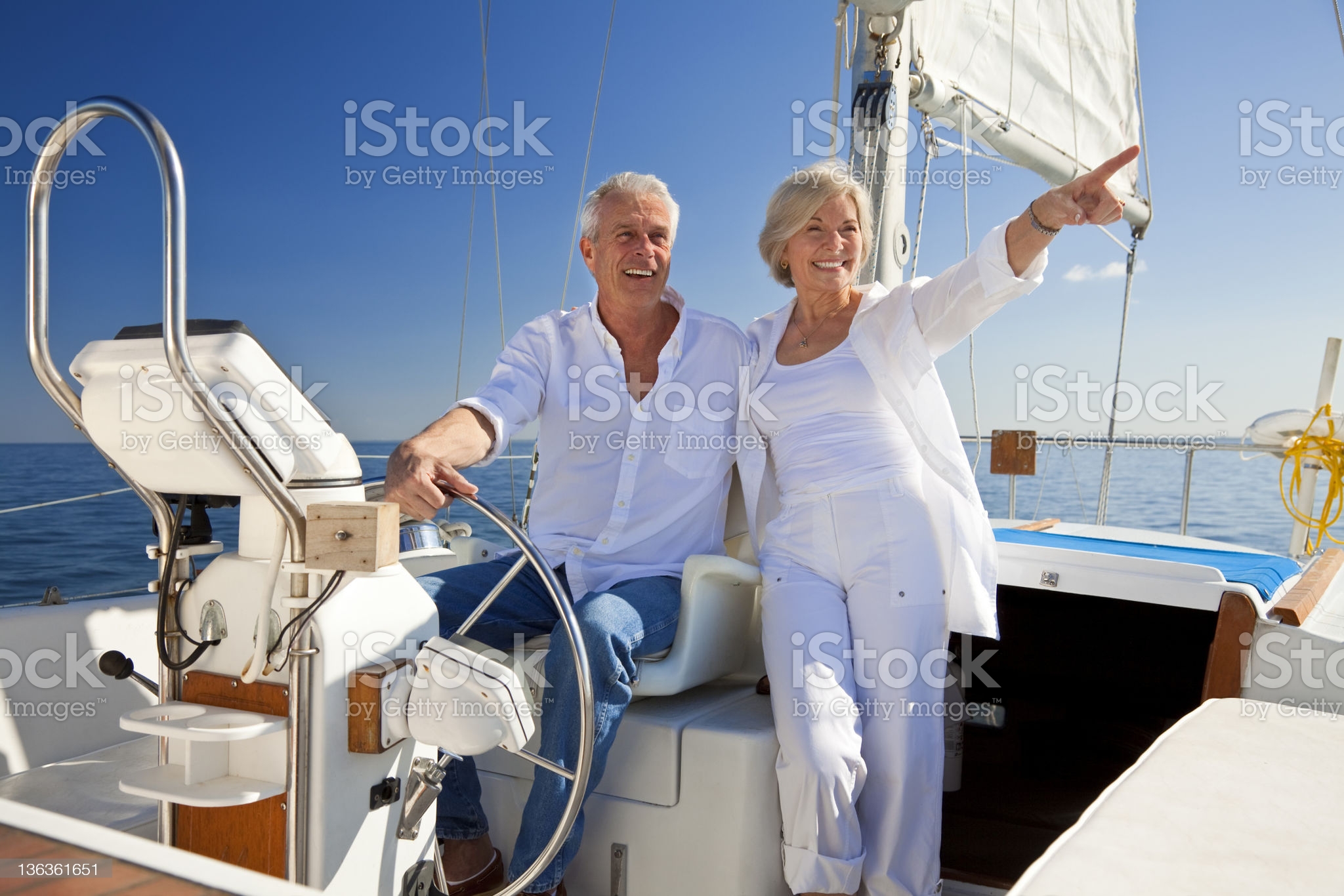 A happy senior couple sitting at the wheel of a sail boat on a calm blue sea